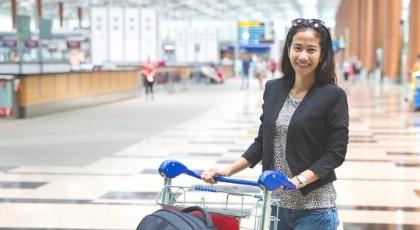 A smiling woman stands with a luggage trolley in an airport