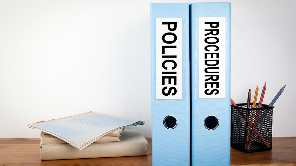Desk scene with binders labelled 'Policies' and 'Procedures'