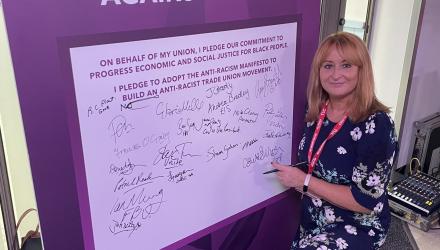 Claire sullivan kneels to sign a large pledge card, already containing a number of handwritten signatures.
