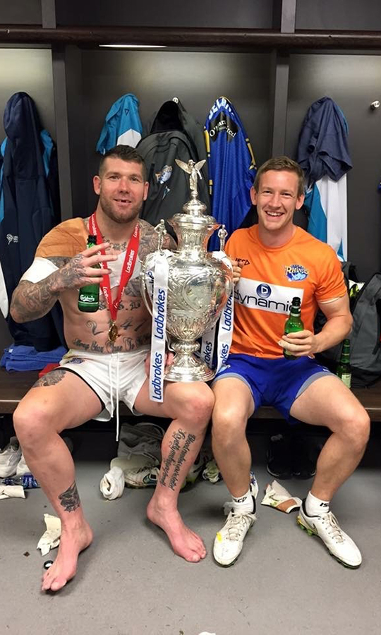 Physio Andy Barker posing with a trophy and sports player in a changing room