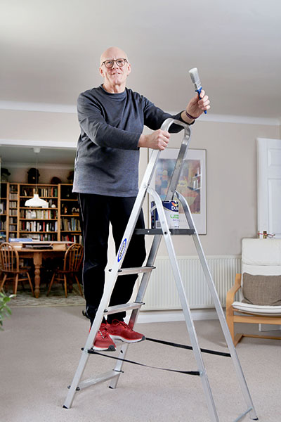 An older man up a ladder with a paintbrush in his hand