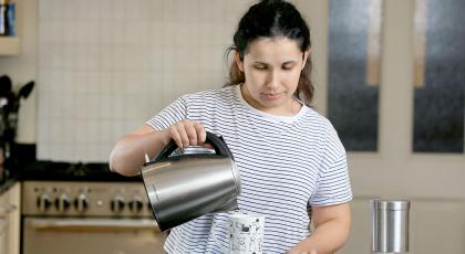 A woman pouring water from a kettle into a mug of tea