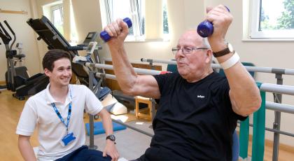 Physio working with a cancer patient and supervising him lifting small handweights