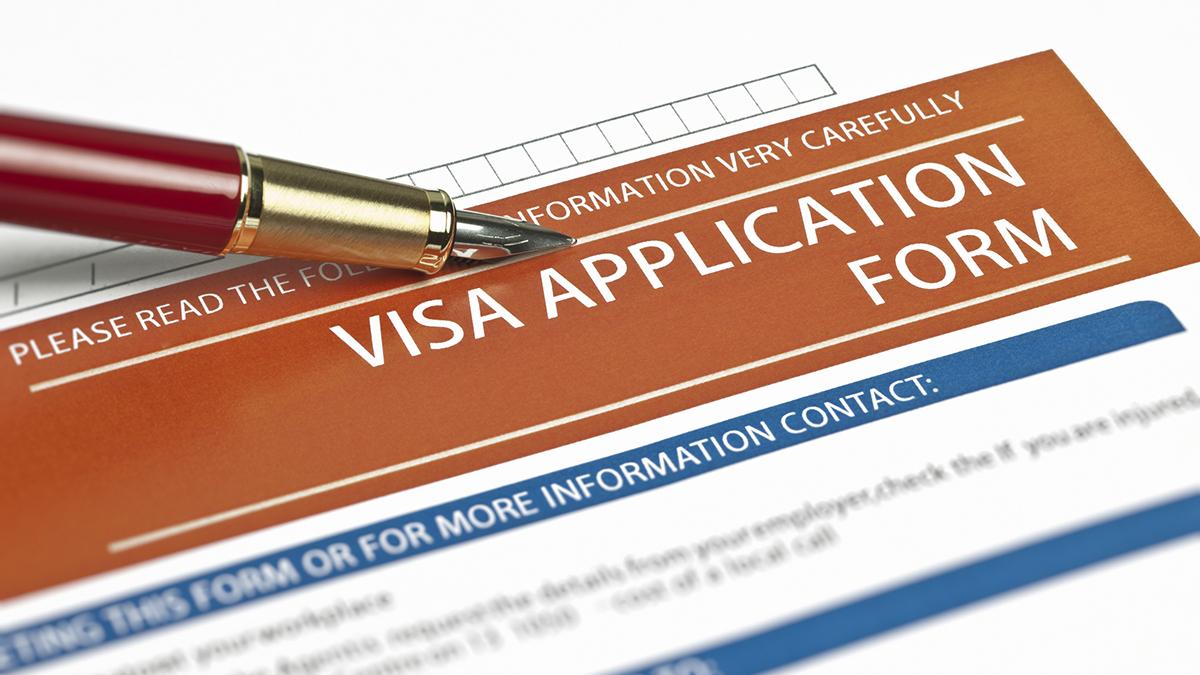 A pen lies across a paper application form for a visa