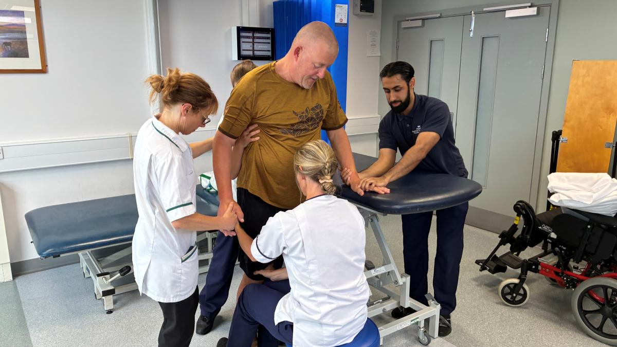 A stroke patient is assisted by four physiotherapists to take his first steps