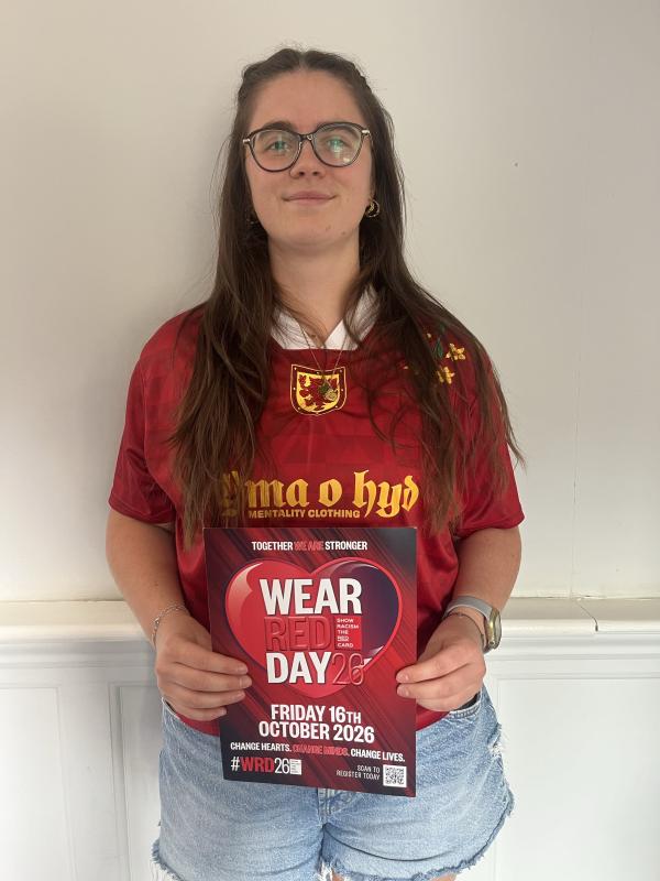 Woman with brown long hair wearing a red top and holding a red poster advertising wear red day