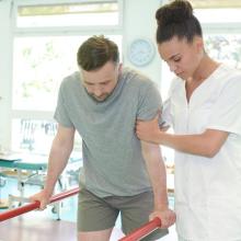 Practitioner helping a patient to support themselves on bars